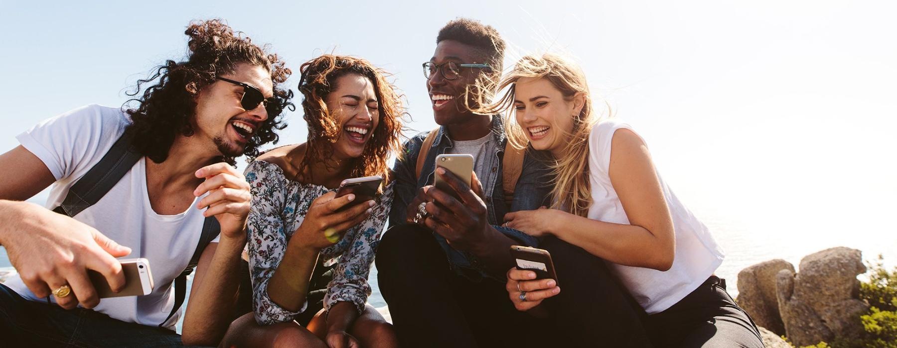 a group of friends sit outside laughing over their cell phones