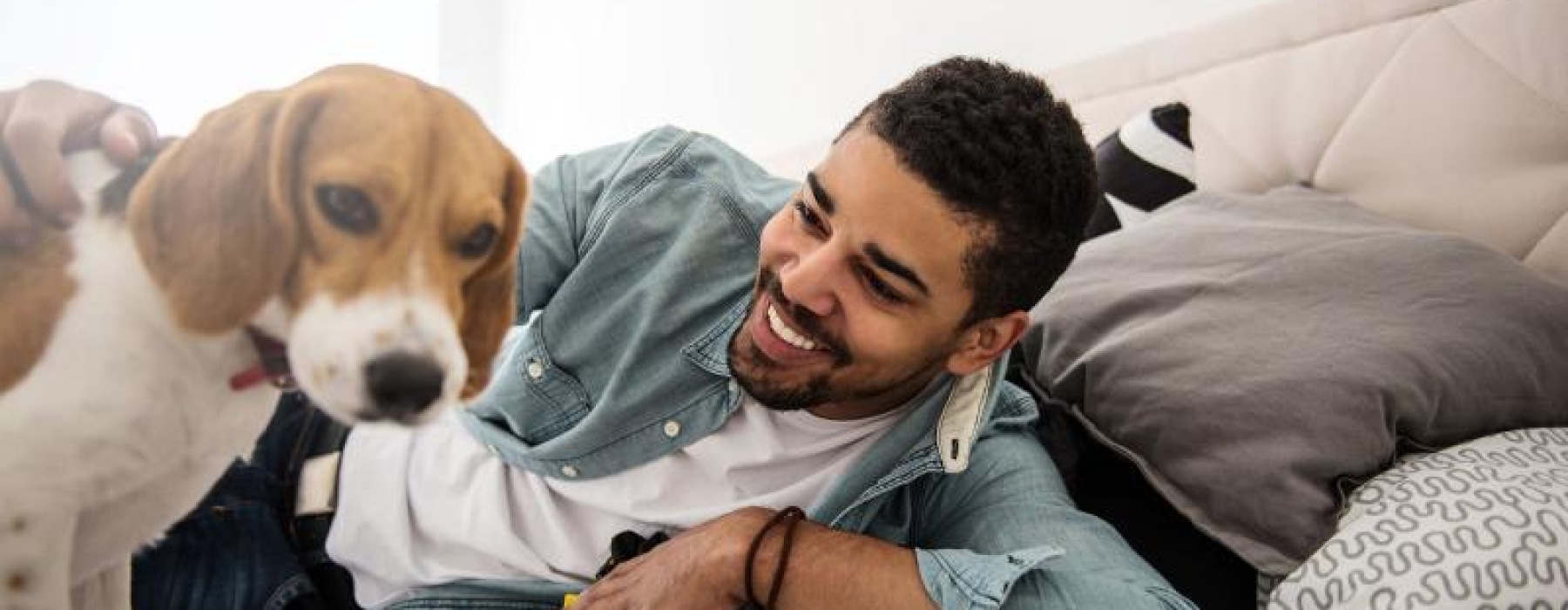 man smiles and pets his dog on a bed