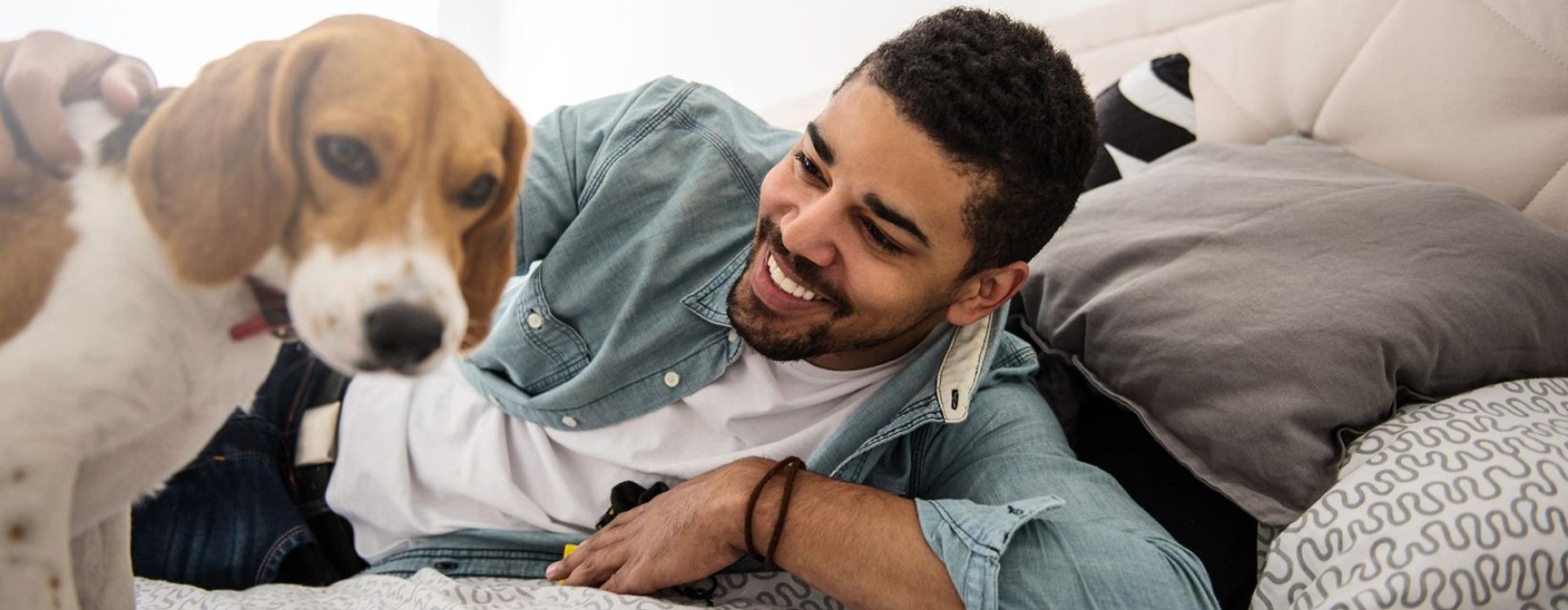 man smiles and pets his dog on a bed